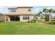 A spacious backyard featuring lush grass, a covered patio, and young palm trees providing a tropical ambiance at 3488 Great Banyan Way, Wesley Chapel, FL 33543