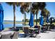 Outdoor patio dining space with wicker chairs, blue umbrellas, and a picturesque waterfront view at 2617 Cove Cay Dr # 401, Clearwater, FL 33760