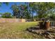 Large backyard with a wood fence, lush green grass, mature shade trees, and a rustic fire pit area at 267 Broad St, Brooksville, FL 34604