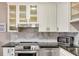 Bright kitchen with white cabinets, glass-front display cabinets, stainless steel appliances, and marble backsplash at 701 38Th N Ave, St Petersburg, FL 33704