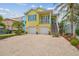 Bright yellow two-story home with a brick driveway, two-car garage, and lush tropical landscaping at 1326 Apollo Beach S Blvd, Apollo Beach, FL 33572
