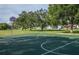 Community basketball court with green surface, white lines, and red hoop surrounded by lush greenery under a bright, partly cloudy sky at 128 Torrington St, Port Charlotte, FL 33954