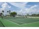 Outdoor tennis court with green surface and net, surrounded by fencing and palm trees at 128 Torrington St, Port Charlotte, FL 33954