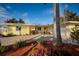 Charming single-story yellow home featuring a brick driveway, lush landscaping, and an attached two-car garage at 2487 W Bay Isle Se Dr, St Petersburg, FL 33705