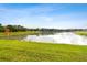 Scenic view of a calm pond surrounded by lush greenery and a clear blue sky, showcasing the natural beauty of the property at 38190 Shale Stone Ct, Zephyrhills, FL 33540