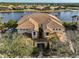 Aerial view of a waterfront condo with a clay tile roof, lush landscaping, and serene lake views at 1348 Emerald Dunes Dr, Sun City Center, FL 33573