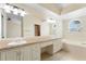 Bright bathroom featuring a double sink vanity, soaking tub, and arched window letting in natural light at 14506 Alejo Ct, Seminole, FL 33776