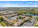 Aerial view showcasing the townhouse community, pool, parking, and nearby lake with expansive blue skies above at 1577 Chateaux De Ville Ct, Clearwater, FL 33764