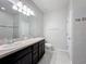Bathroom featuring double sinks, dark vanity, tiled floor, toilet, and a framed mirror at 15579 Stone House Dr, Brooksville, FL 34604