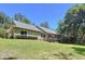 Rear of the home with a well-kept lawn, mature trees, gray roof, and wooden deck at 16224 Iola Woods Trl, Dade City, FL 33523