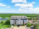 Aerial view of a multi-story building with beautiful landscaping, nearby golf course, water, and blue skies at 14820 Rue De Bayonne # 208, Clearwater, FL 33762