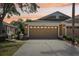 Charming home at sunset featuring a large garage door, mature landscaping and exterior lighting at 19129 Lake Audubon Dr, Tampa, FL 33647