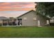 Spacious backyard showcasing a screened lanai, lush lawn, and a neutral-toned exterior with arched windows under an orange sunset at 4511 Swift Cir, Valrico, FL 33596