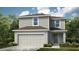 Two-story home featuring a two-car garage, gray siding, and a cozy front porch surrounded by lush landscaping at 13273 Tropical Breeze Way, Hudson, FL 34669