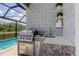Outdoor kitchen featuring stainless steel grill, stone accents, patterned tile backsplash and shelves, near pool at 2826 Riders Pass, Odessa, FL 33556