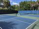 Close up of a blue and green tennis court with fences and net, set against a backdrop of lush trees at 829 E Gulf Blvd # 107, Indian Rocks Beach, FL 33785