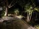Outdoor patio with dining table and lush tropical landscaping at night with landscape lighting at 1750 Arabian Ln, Palm Harbor, FL 34685