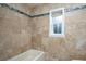 Bathroom featuring tub and shower with travertine tile from floor to ceiling and a window at 2675 Firestone Dr, Clearwater, FL 33761