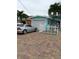 Charming teal home featuring a garage, brick driveway, and neatly maintained yard with tropical palm trees at 14555 N Bayshore Dr, Madeira Beach, FL 33708