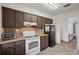 Well-lit kitchen featuring wooden cabinets, tile flooring, white appliances, and an open doorway at 20413 Keene Rd, Wimauma, FL 33598