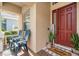 Inviting front porch with brick-patterned flooring, seating, and a charming 'Hello' welcome mat at the red front door at 30817 Pumpkin Ridge Dr, Wesley Chapel, FL 33543