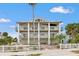 An exterior view features a three-story coastal home, with multiple balconies, a white picket fence, and lush palms at 1104 Pass A Grille Way, St Pete Beach, FL 33706