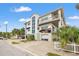 An exterior view of a three-story coastal home with a garage, multiple balconies, and lush tropical landscaping at 1104 Pass A Grille Way, St Pete Beach, FL 33706