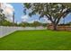 Large backyard with lush green grass, mature trees, and a white vinyl fence at 3616 W Platt St, Tampa, FL 33609