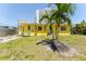 Exterior of the home featuring small green backyard and bright yellow paint and large palm trees at 6750 Hibiscus S Ave, South Pasadena, FL 33707