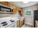 Galley kitchen featuring light wood cabinets, white appliances, stone countertops, and a garden window at 1980 Taylor Lake Cir, Largo, FL 33778