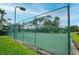A well-maintained community tennis court featuring a green surface, surrounded by a secure green fence, trees and manicured landscaping at 3177 Montrose Pl, Palm Harbor, FL 34684