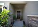 A welcoming covered front porch area featuring potted plants and a decorative wall lamp at 19047 Alfaro Loop, Spring Hill, FL 34610