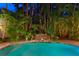 Night view of pool featuring lush tropical landscaping and stacked stone waterfall with a vibrant, turquoise hue at 2714 W Jetton Ave, Tampa, FL 33629