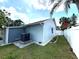 Light blue home's backyard featuring green grass, a white fence, palm trees, and an AC unit at 11303 Hollyglen Dr, Tampa, FL 33624