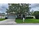 Charming single-story home featuring a well-manicured lawn, mature tree, and gray siding with an attached two-car garage at 29042 Rivergate Run, Wesley Chapel, FL 33543