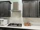 Modern kitchen showcases a stainless steel range hood, gas cooktop, dark cabinets, and elegant white quartz backsplash at 29042 Rivergate Run, Wesley Chapel, FL 33543