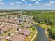An aerial view shows homes near a lake with manicured lawns and a lush green wooded area at 30327 Lettingwell Cir, Wesley Chapel, FL 33543
