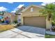 Tan home featuring a brown garage door, palm tree, well manicured lawn and a sunny sky at 30327 Lettingwell Cir, Wesley Chapel, FL 33543