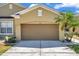 Tan home featuring a brown garage door, a palm tree, well manicured lawn and a sunny sky at 30327 Lettingwell Cir, Wesley Chapel, FL 33543