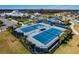 Aerial view of pristine tennis courts with covered seating areas, surrounded by palm trees and manicured landscaping at 5670 Shorebird Br, Land O Lakes, FL 34638