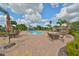 Community pool with lounge chairs and tables around a brick-paved patio, surrounded by lush landscaping and palm trees at 7657 Nottinghill Sky Dr, Apollo Beach, FL 33572