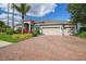 Paver driveway leads to a meticulously landscaped home with a three-car garage under a clear blue sky at 26701 Winged Elm Dr, Wesley Chapel, FL 33544