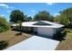 Well-maintained single-story home with a white metal roof, gray exterior, and a spacious driveway leading to a two-car garage at 30456 Willow Bank Ave, Brooksville, FL 34602