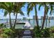 Picturesque waterfront view featuring a private dock framed by lush greenery and swaying palm trees against the serene water at 755 Bay Esplanade, Clearwater Beach, FL 33767