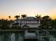 Waterfront home featuring multiple stories, balconies, dock, and palm trees at sunset at 755 Bay Esplanade, Clearwater Beach, FL 33767