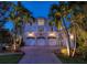 Exterior shot of the garage featuring three doors, lush landscaping, and exterior lighting at twilight at 755 Bay Esplanade, Clearwater Beach, FL 33767