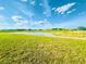 A sprawling backyard with lush green grass leads down to a tranquil pond, all under a bright blue, partly cloudy sky at 11257 Linden Depot Rd, San Antonio, FL 33576