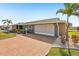 Attractive home featuring a large two-car garage, lush landscaping, and a brick-paved driveway at 1405 W Del Webb Blvd, Sun City Center, FL 33573