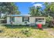 Exterior view of single story white home with green shutters and blue tarp roof surrounded by unkempt yard at 4815 N Falkenburg Rd, Tampa, FL 33610