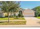 Charming single-story home featuring a well-manicured lawn, mature tree, and a two-car garage at 16616 Magnolia Reserve Pl, Wimauma, FL 33598
